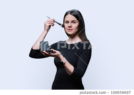 Young woman holding powder and using makeup brush, on white background Young woman holding powder and using makeup brush, on white background 100656697