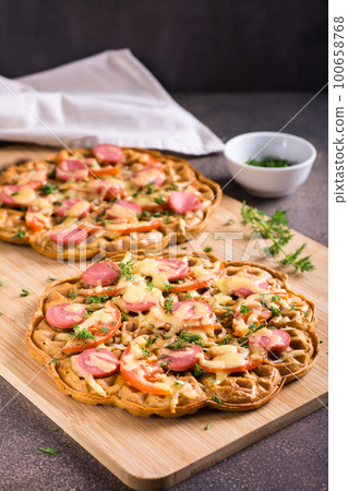 Waffle pizza with tomatoes, sausages, cheese and herbs on a wooden board. Vertical view Waffle pizza with tomatoes, sausages, cheese and herbs on a wooden board. Vertical view 100658768