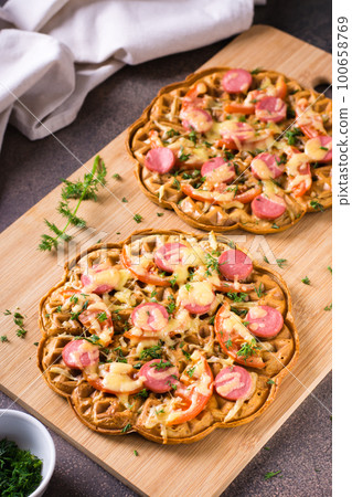 Appetizing pizza waffle with vegetables, sausages and cheese on a board on the table. Vertical view Appetizing pizza waffle with vegetables, sausages and cheese on a board on the table. Vertical view 100658769
