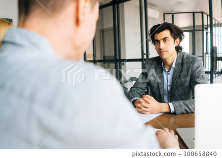 View from back of unrecognizable man from human resources department is interviewing businessman candidate for job application in meeting room while considering CV resume document. View from back of unrecognizable man from human resources department is interviewing businessman candidate for job application in meeting room while considering CV resume document. 100658840