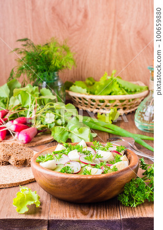 Delicious spring vegetable salad from cucumber, radish, quail eggs, herbs and oil in a plate on a wooden table 100659880