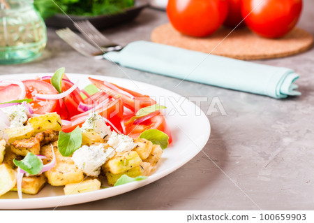 Fried zucchini with feta cheese, tomatoes, herbs and onions on a plate on a table Fried zucchini with feta cheese, tomatoes, herbs and onions on a plate on a table 100659903
