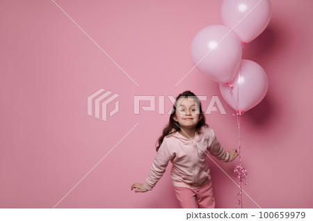 Adorable Caucasian little girl holding bunch of inflatable pink pastel balloons, isolated over color pink background. International Children's day. Celebrating festive events. Copy advertising space 100659979