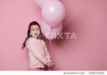 Lovely little child girl holding a bunch with inflatable pink pastel balloons, isolated on pink color background, confidently looking at camera. Emotions. Kids. International Children's day concept Lovely little child girl holding a bunch with inflatable pink pastel balloons, isolated on pink color background, confidently looking at camera. Emotions. Kids. International Children's day concept 100659984