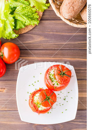 Fresh tomatoes baked with cheese and egg sprinkled with green onions on a plate on a wooden table. Top view. Copy space 100660076