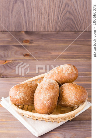 Fresh rye buns in a basket on a wooden table 100660078