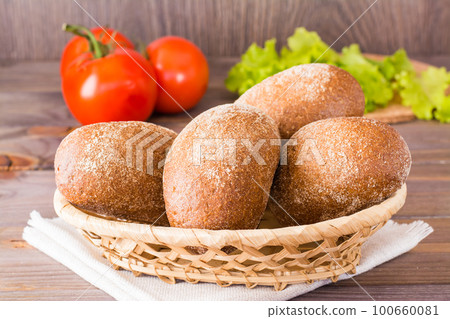 Fresh rye buns in a basket, salad and tomato on a wooden table 100660081