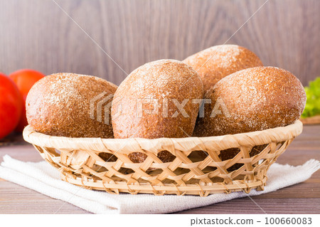 Fresh rye buns in a basket, salad and tomato on a wooden table 100660083