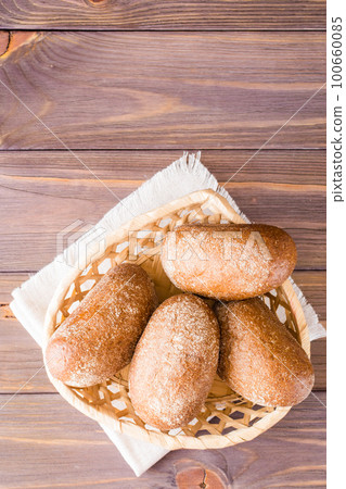 Fresh rye buns in a basket on a wooden table. Top view. Copy space 100660085
