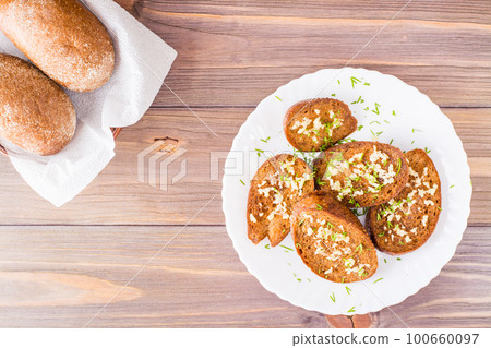 Fresh rye garlic croutons with dill on a plate and buns in a basket on a wooden table. Top view. Copy space 100660097