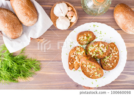 Fresh rye garlic croutons with dill on a plate and buns in a basket on a wooden table. Top view. Fresh rye garlic croutons with dill on a plate and buns in a basket on a wooden table. Top view. 100660098