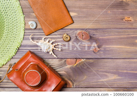 Camera in a case, passport, hat and seashells on a wooden background. Retro style. Place for the inscription. Vacation concept. Camera in a case, passport, hat and seashells on a wooden background. Retro style. Place for the inscription. Vacation concept. 100660100