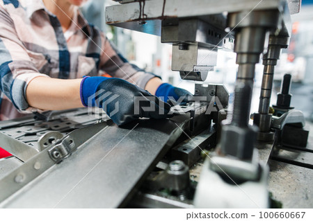 Woman worker in factory producing parts on punching machine Woman worker in factory producing parts on punching machine 100660667