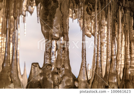 Icicles in cave on Baikal lake at sunset 100661623