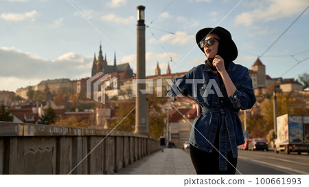 Stylish beautiful young woman earing black hat in Prague on a bridge with Prague Castle or Prazsky Hrad on background. Elegant retro lady fine art portrait. Stylish beautiful young woman earing black hat in Prague on a bridge with Prague Castle or Prazsky Hrad on background. Elegant retro lady fine art portrait. 100661993