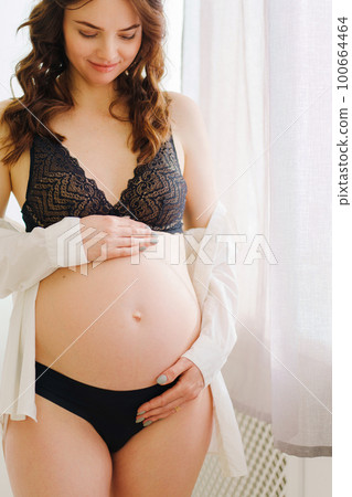 a beautiful pregnant woman in a black underwea and white shirt by the window a beautiful pregnant woman in a black underwea and white shirt by the window 100664464