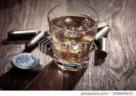 Whisky shot with ice and ammunitions with old silver dollars coins on wooden table Whisky shot with ice and ammunitions with old silver dollars coins on wooden table 100664635