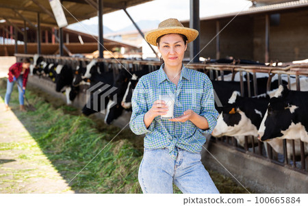Portrait of a positive kazakh farmer woman in a cowshed, holding a glass of milk 100665884