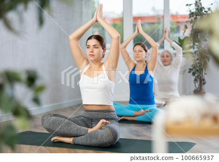 Diligent women practicing lotus pose of yoga in light fitness room Diligent women practicing lotus pose of yoga in light fitness room 100665937