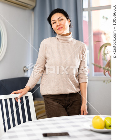 Woman standing at table in apartment, posing and looking at camera Woman standing at table in apartment, posing and looking at camera 100666016