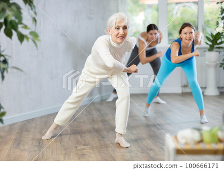 Cheerful senior woman training zumba with group Cheerful senior woman training zumba with group 100666171