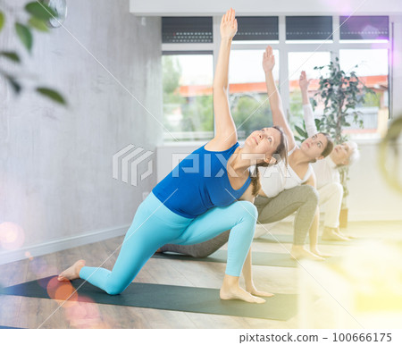Diligent women practicing triangle pose of yoga in light fitness room Diligent women practicing triangle pose of yoga in light fitness room 100666175