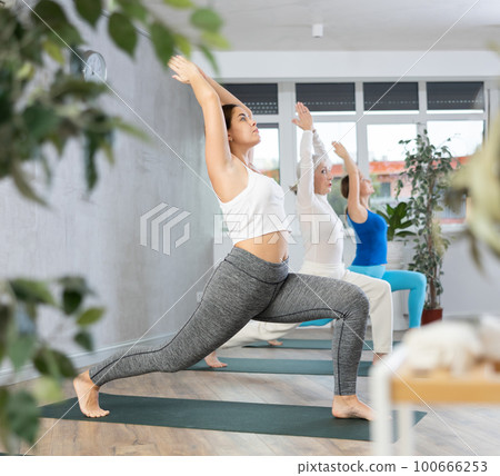 Young focused women doing crescent moon pose in yoga studio 100666253