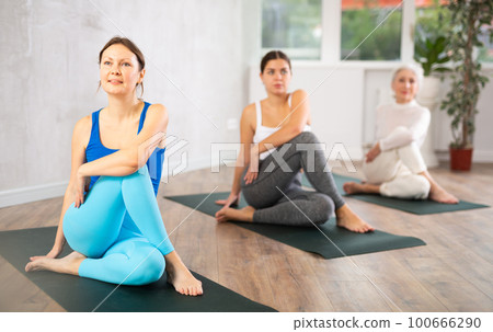 Young female yoga instructor showing others sage pose in wellness center 100666290