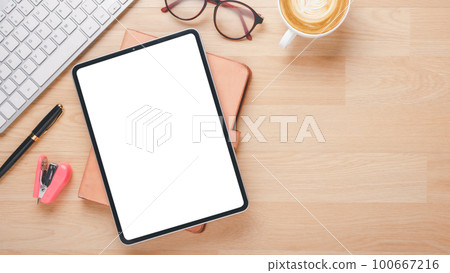 Wooden desk workplace with blank screen tablet, keyboard, notebook, eyeglass, pen and cup of coffee, Top view flat lay with copy space. 100667216