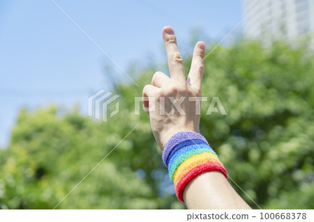 戴著彩虹色腕帶的男人手的和平標誌 戴著彩虹色腕帶的男人手的和平標誌 100668378