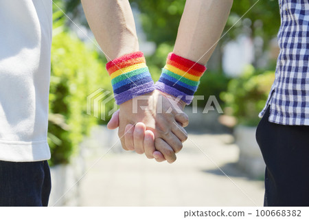 Hands of a male couple holding hands with a rainbow-colored wristband Hands of a male couple holding hands with a rainbow-colored wristband 100668382