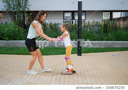 Mother helps daughter learn to roller skate. Mother helps daughter learn to roller skate. 100670285