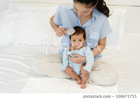 mother combing her newborn baby hair on bed mother combing her newborn baby hair on bed 100671755