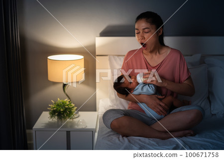 sleepy mother yawning and feeding milk bottle to newborn baby on bed at night sleepy mother yawning and feeding milk bottle to newborn baby on bed at night 100671758