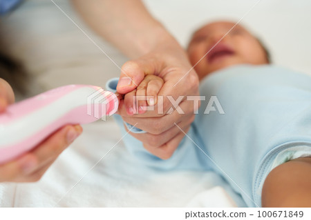 mother cutting baby's fingernails with auto electic nail trimmer. 100671849