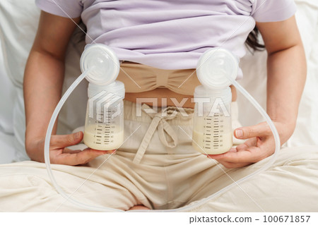 mother using breast pump machine to pumping milk for her newborn baby on bed 100671857