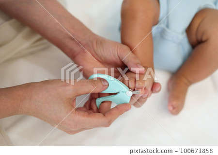 mother cutting baby's foot fingernails with nail scissors. 100671858