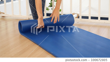 Woman hands rolled up yoga mat on gym floor in yoga fitness training room. Home workout woman close up hands rolling foam yoga gym mat. Woman barefoot home workout sportive healthy lifestyle concept 100672805