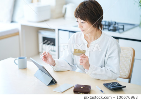 A woman holding a card and operating a tablet PC A woman holding a card and operating a tablet PC 100676968