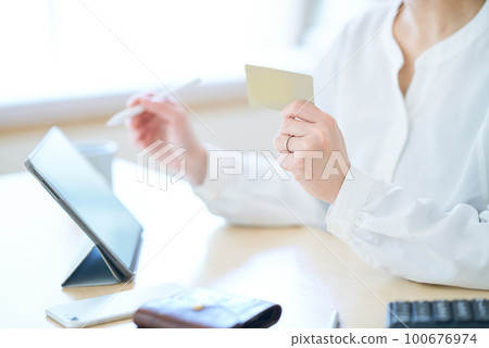 A woman holding a card and operating a tablet PC 100676974