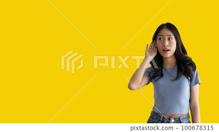Asian woman eavesdropping or overhearing secret conversation isolated on yellow background, Gossip, Listening, Yellow background studio portrait. Asian woman eavesdropping or overhearing secret conversation isolated on yellow background, Gossip, Listening, Yellow background studio portrait. 100678315