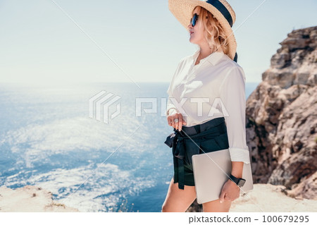 Woman sea laptop. Business woman in yellow hat freelancer with laptop working over blue sea beach. Girl relieves stress from work. Freelance, digital nomad, travel and holidays concept 100679295
