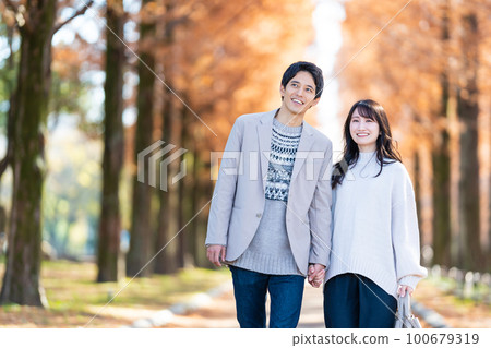 年輕夫婦手牽手走在綠樹成蔭的街道上 100679319