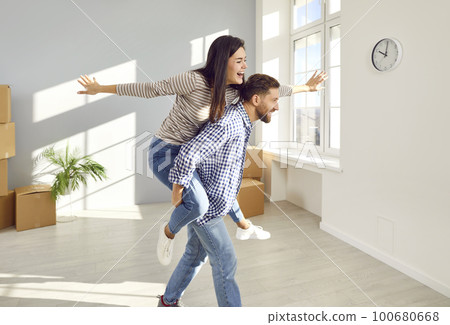 Happy young woman riding on her boyfriend's back celebrating moving day in their new appartment. Happy young woman riding on her boyfriend's back celebrating moving day in their new appartment. 100680668