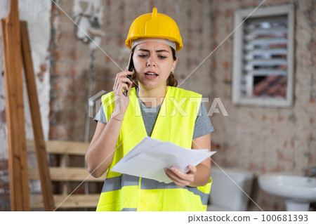 Young woman civil engineer with papers talking on phone at construction site Young woman civil engineer with papers talking on phone at construction site 100681393