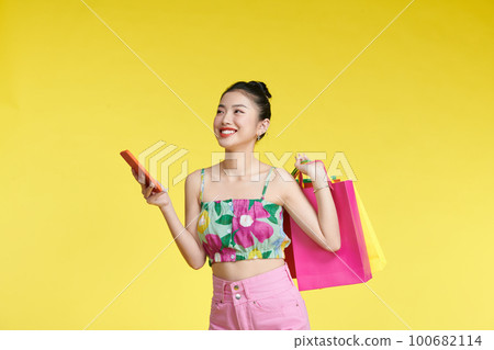happy young asian woman celebrating with mobile phone and holding shopping bags happy young asian woman celebrating with mobile phone and holding shopping bags 100682114