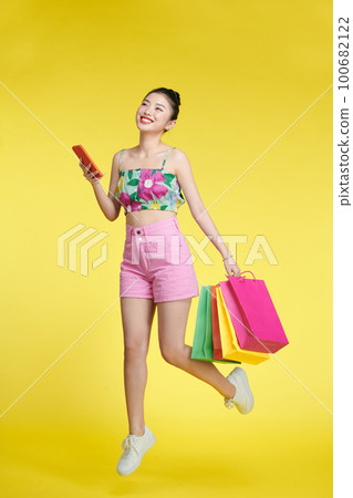 Full length of happy young attractive shopaholic woman raising shopping bags and holding mobile phone 100682122