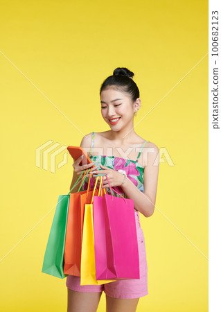 Portrait of a young woman using mobile phone with shopping bags in her hands. 100682123