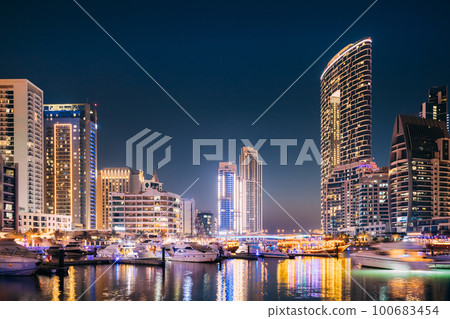 Beautiful Night View Of Dubai Marina Skyline. Yachts Moored Near City Pier, Jetty In Evening Night Illuminations Beautiful Night View Of Dubai Marina Skyline. Yachts Moored Near City Pier, Jetty In Evening Night Illuminations 100683454