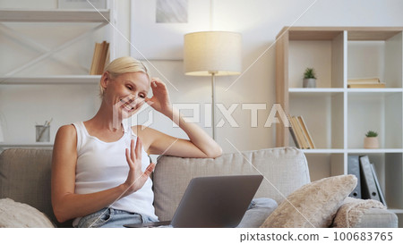 Web chat. Video meeting. Online communication. Relaxed happy smiling senior woman waving hi enjoying fun conversation using laptop on couch at home interior with free space. Web chat. Video meeting. Online communication. Relaxed happy smiling senior woman waving hi enjoying fun conversation using laptop on couch at home interior with free space. 100683765